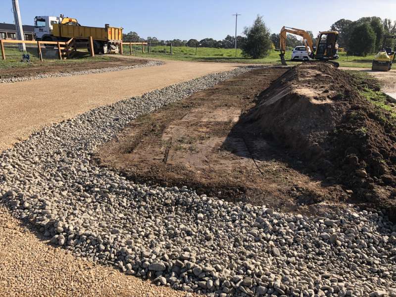 Mini excavator digging a precise drainage trench alongside a gravel driveway in central Victoria ensuring correct slope.